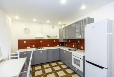 Kulübedeki modern stil büyük mutfak. Mutfak kırmızı ve çelik renklerde. Kapılar çelik renkli ve duvardaki fayanslar kırmızı. Döşeme kiremitleri bej. Dört sandalyeli beyaz masa..