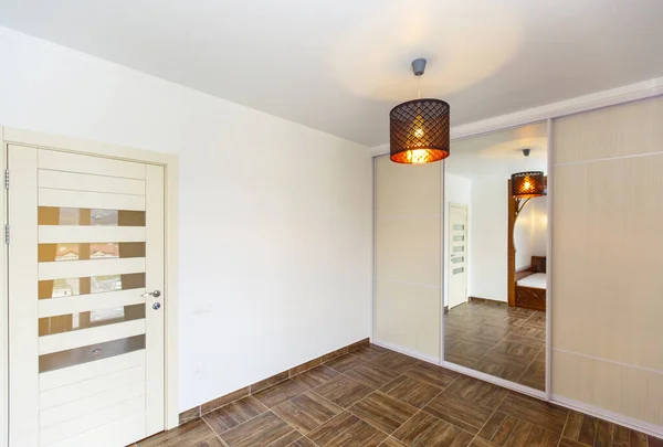 Corner of the room with a mirror in the closet, door, chandelier and beige tiles on the floor