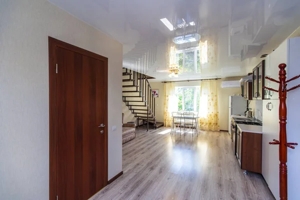 Kitchen in the guest house. Wooden furniture made of dark wood. Refrigerator, washing machine. Wooden staircase to the second floor. Sofa under the stairs