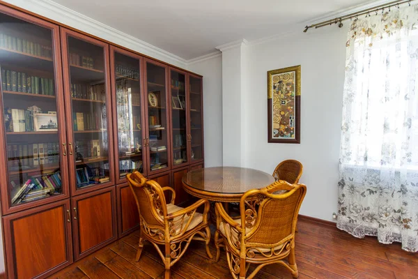 Biblioteca domestica. Grande libreria con libri. un tavolo di vimini e quattro sedie. Parquet in legno — Foto Stock