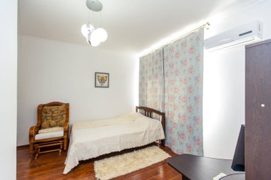 Güneşli oda, çift katlı ahşap bir yatak, sallanan bir sandalye ve yatağın yanında tüylü bir halı.