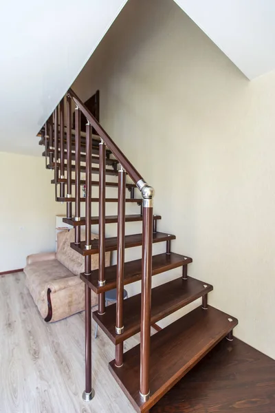 Eine Holztreppe aus dunklem Holz mit einem glänzenden runden vernickelten Geländer. Eine Treppe führt vom Speisesaal im ersten Stock des Gästehauses in den zweiten Stock — Stockfoto