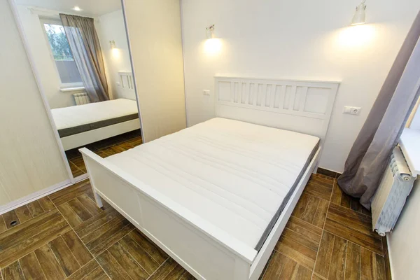 Camera da letto in colori bianchi in casa. Ampio letto matrimoniale bianco, grande specchio sull'armadio scorrevole, pavimento in parquet beige — Foto Stock