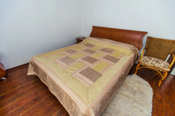マホガニーベッド、ウィッカーチェア、半円形の鏡を備えたエレガントなドレッシングテーブルを備えた大きなベッドルーム。ベッドは正方形にベージュの毛布を持っています。マホガニーの寄木細工 — ストック写真