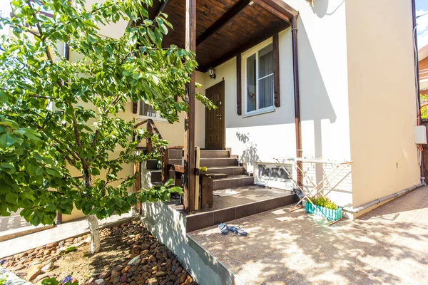 Porch, steps and entrance to the cottage in the back yard of the house. Canopy over the entrance. Shoes on the porch. Backyard with trees. Sunny day. — Stock Photo, Image