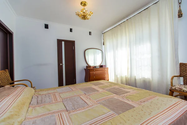 Ein großes Schlafzimmer mit einem Mahagoni-Bett, Korbstühlen und einem eleganten Schminktisch mit einem halbrunden Spiegel. Das Bett hat eine beige Decke in Quadraten. Mahagoni-Parkett — Stockfoto