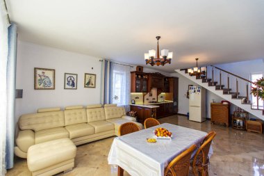 Klasik parlak oturma odası. Evde ahşap mobilyalar var. Ortasında meyveli bir masa ve dört hasır sandalye var. Beyaz deri kanepe. Tahtadan yapılma antika Yan Tahta. 