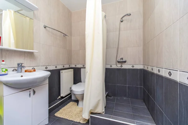 Fürdőszoba a vendégházban. Bézs cserép a tetején, sötét cserép az alján. Zuhanyozó és mosogató — Stock Fotó