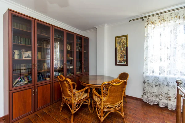 Biblioteca domestica. Grande libreria con libri. un tavolo di vimini e quattro sedie. Parquet in legno — Foto Stock