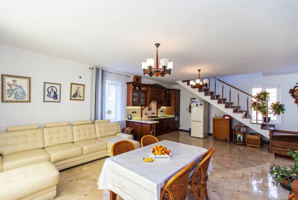 Klasický světlý obývací pokoj s dřevěným nábytkem v domě. Uprostřed je stůl s ovocem a čtyřmi proutěnými židlemi. Bílá velká kožená pohovka. Starožitná postranní deska ze dřeva. — Stock fotografie