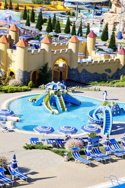 Aquapark, çocukların su kayakları ve binişleri. Şemsiyeler ve güneş yatakları havuzun kenarında.