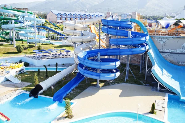 Water Park on the beach on a Sunny morning. Rides in the form of spiral pipes. There are channels with running water at the bottom. Striped blue umbrellas, white sun beds — Stock Photo, Image