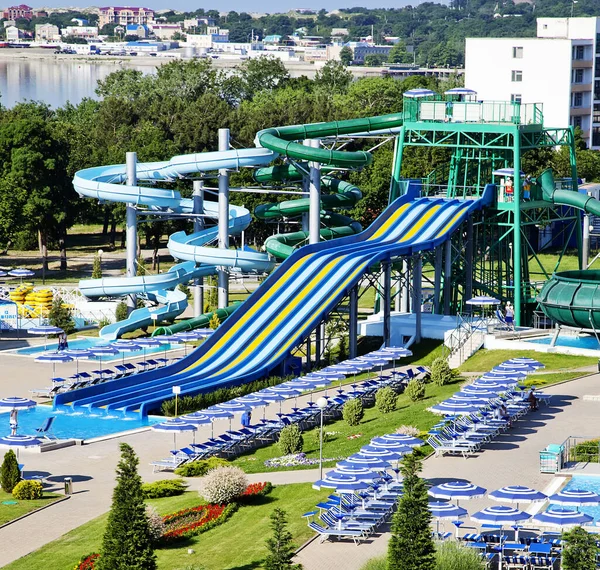 Aquapark na pláži za slunečného rána. Prudké vícebarevné skluzavky a jezírko na dně. Atrakce ve formě spirálních trubek — Stock fotografie