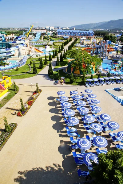 Zentrale Gasse des Wasserparks an einem sonnigen Tag. Rutschen und Fahrgeschäfte rund ums Wasser. Sonnenschirme und Liegestühle am Beckenrand — Stockfoto