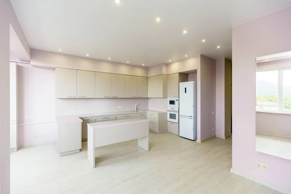 Nuovi mobili da cucina in colori bianchi nello stile del minimalismo in un nuovo edificio. muro rosa. elettrodomestici da cucina: frigorifero, piano cottura a gas con forno. Tavolo di fronte alla cucina — Foto Stock