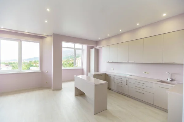Una grande stanza con pareti rosa e un set da cucina bianco. Mobili da cucina è nuovo con tutti gli elettrodomestici da cucina. Davanti alla cucina c'è un tavolo bianco. Fresco, nuova ristrutturazione . — Foto Stock