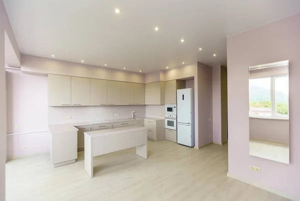 Ein großer Raum mit rosa Wänden und einem weißen Küchenset. Die Küchenmöbel sind bei allen Küchengeräten neu. Vor der Küche steht ein weißer Tisch. Frische, neue Renovierung. — Stockfoto