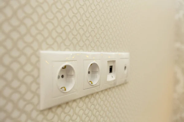 Three electrical outlets on the wall against a background of sand colored Wallpaper with a pattern of oval lines — Stock Photo, Image