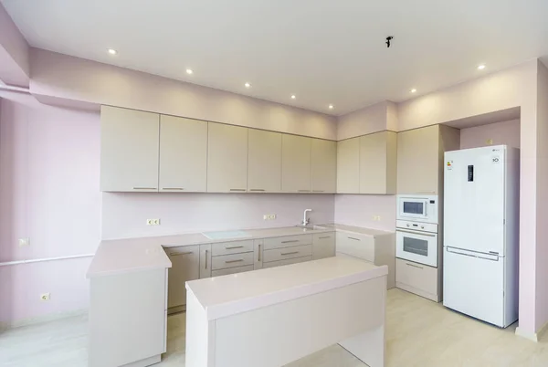 Neue Küchenmöbel in weißen Farben im Stil des Minimalismus in einem neuen Gebäude. rosa Wand. Küchengeräte: Kühlschrank, Gasherd mit Backofen. Tisch vor der Küche — Stockfoto