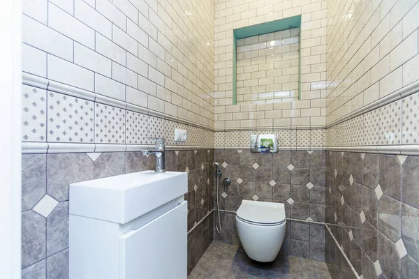 A narrow toilet with a toilet bowl and a small sink. Beige tiles on the walls and dark beige closer to the floor — Stock Photo, Image