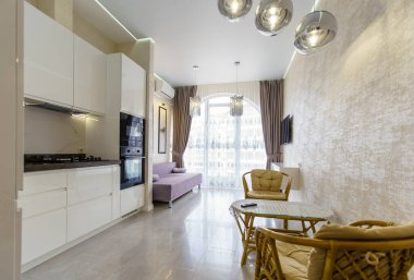 Mutfak odası, bej renginde yenilenmiş. Mutfak aletleriyle dolu beyaz mutfak seti. Perdeli yarı dairesel pencere. Televizyon, kanepe, hasır mobilya masası ve iki sandalye.