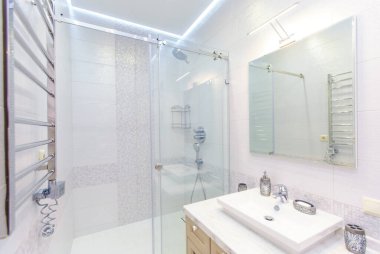 Zarif dikdörtgen lavabosu, tuvaleti ve duşu olan banyo. Tepesinde ışık olan ayna. Beyaz fayans..