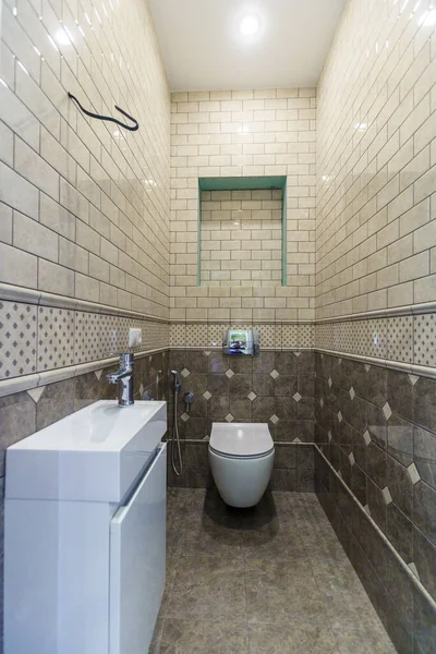 Egy keskeny vécé WC-csészével és egy kis mosogatóval. Bézs csempék a falakon és sötét bézs közelebb a padlóhoz — Stock Fotó