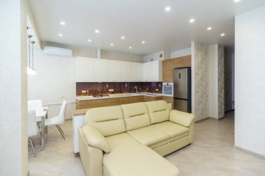 Konforlu mutfak oturma odası ve yeni bir yenileme. Ortadaki beyaz deri kanepe. Ahşap tabanlı mutfak seti ve beyaz üst dolaplar. Buzdolabı, gaz sobası..