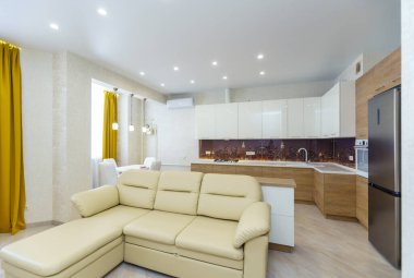 Konforlu mutfak oturma odası ve yeni bir yenileme. Ortadaki beyaz deri kanepe. Ahşap tabanlı mutfak seti ve beyaz üst dolaplar. Buzdolabı, gaz sobası..