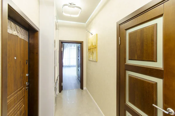 A long corridor in the apartment with beige Wallpaper, numerous doors and light yellow abstract paintings on the walls — Stock Photo, Image