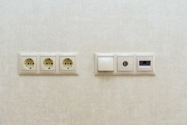Three electrical outlets on the wall against a background of sand colored Wallpaper with a pattern of oval lines — Stock Photo, Image