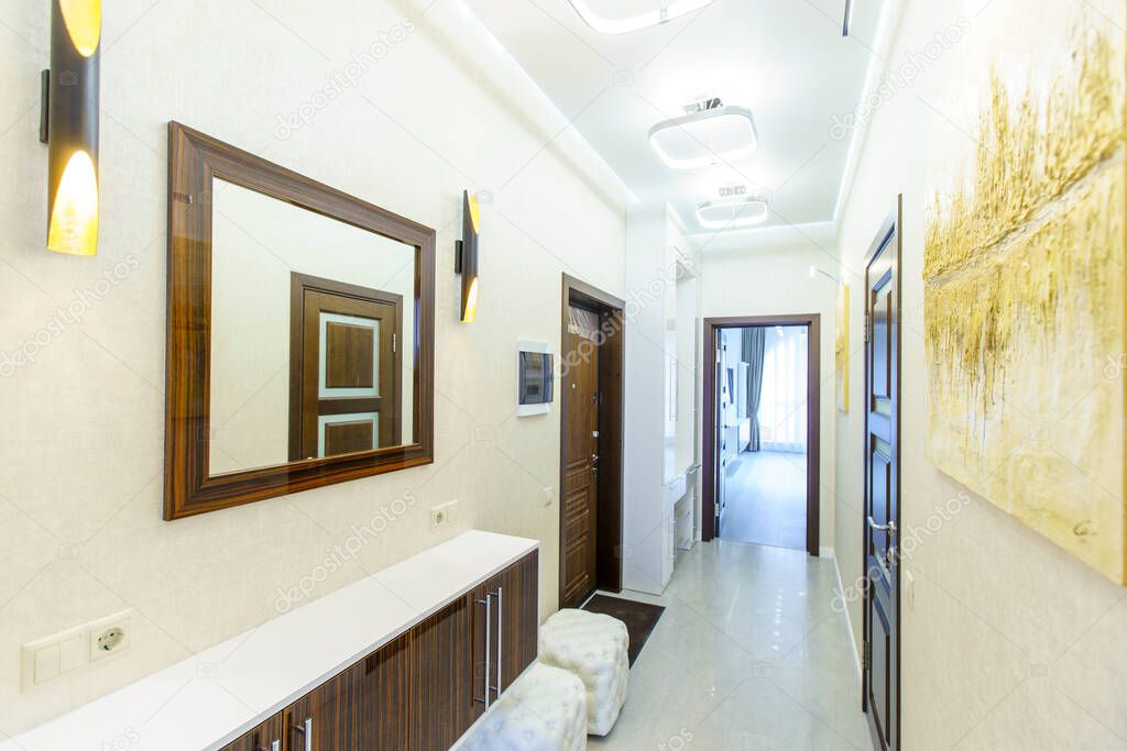 a long corridor in the apartment with beige Wallpaper, numerous doors and light yellow abstract paintings on the walls