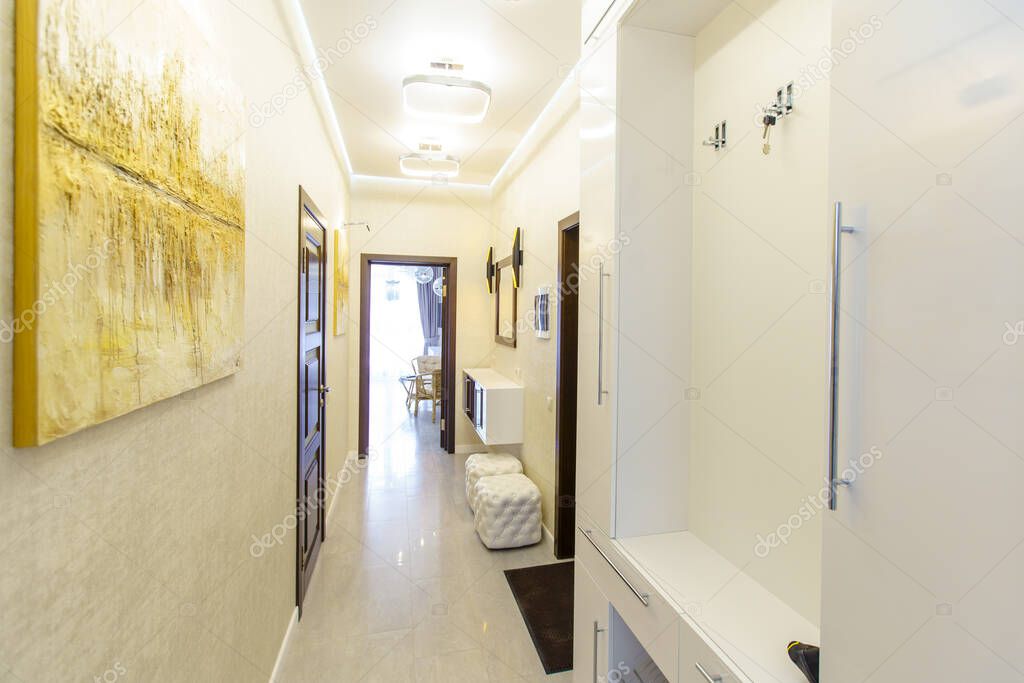 a long corridor in the apartment with beige Wallpaper, numerous doors and light yellow abstract paintings on the walls