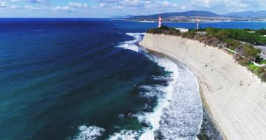 Karadeniz kıyısı boyunca İHA uçuşu. Yüksek kayalık uçurum. Aşağıda bir kiremit plajı şeridi var. Uzakta, Gelendzhik deniz feneri. 