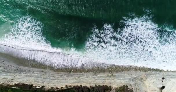 岩の多い海岸の下の小さなビーチで白い泡のロールでサーフィンの波。玉座からの眺め — ストック動画