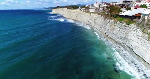 无人机沿着黑海海岸线飞行。高岩石悬崖。下面是一片带状物的海滩。在远方，Gelendzhik灯塔. — 图库视频影像