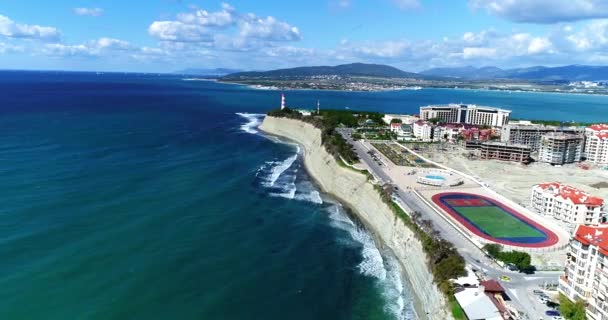 Lot dronem wzdłuż wybrzeża Morza Czarnego. Wysoki skalisty klif. Na dole pasek żwirkowej plaży. W oddali latarnia morska Gelendzhik. — Wideo stockowe