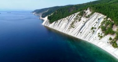 Denizin kayalık kıyısı boyunca ve Karadeniz 'deki Gelendzhik tatil beldesi yakınlarında uçuş. Ağaçlarla kaplı yüksek katmanlı kayalar. Arka planda Blue Bay, Gelendzhik, Kafkasya dağları. Temizle