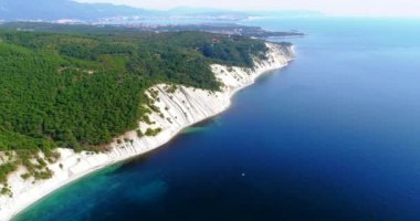 Denizin kayalık kıyısı boyunca ve Karadeniz 'deki Gelendzhik tatil beldesi yakınlarında uçuş. Ağaçlarla kaplı yüksek katmanlı kayalar. Arka planda Blue Bay, Gelendzhik, Kafkasya dağları. Temizle