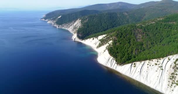 Flug über die Schwarzmeerküste von Gelendschik nach Noworossijsk. Die Drohne fliegt über hoch abfallende Felsen aus geschichtetem Gestein. Die Berge sind mit Kiefern bewachsen. Ein kleiner Kieselstrand am Fuße des — Stockvideo