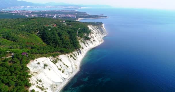 Voo ao longo da costa rochosa do mar e perto do resort de Gelendzhik, Mar Negro. Rochas de camadas altas cobertas de árvores. Ao fundo, a Baía Azul, Gelendzhik, as montanhas do Cáucaso. Claro. — Vídeo de Stock