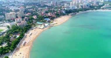 Gelendzhik tatil köyünün merkez plajı kuş bakışı manzaralı. Sıralar dolusu güneş şezlongları ve şemsiyelerle kumlu bir sahilde uçmak. İnsanlar yüzer ve güneşlenir. Gelendzhik 'in güzel zümrüt yeşili suyu