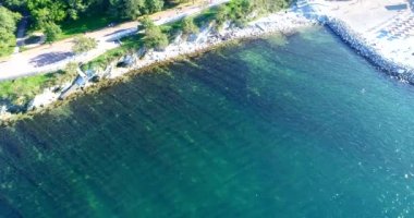 Yazın Gelendzhik tatil beldesi üzerinde uçuş. Kiremit plajı, kiremitli döşeme, kiremit. Temiz su, yosun. Sahilde güneş yatakları ve hasır şemsiyeler var. Kaya parçaları