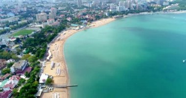 Gelendzhik tatil köyünün merkez plajı kuş bakışı manzaralı. Sıralar dolusu güneş şezlongları ve kumdaki şemsiyeler. İnsanlar yüzer ve güneşlenir. Zümrüt suyu. Sahil boyunca bir kiriş seti var.