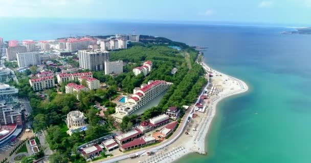 Beach of the resort city of Gelendzhik in the area of Tolstoy Cape. There are rows of sun loungers and straw umbrellas on the pebbly beach. Green tree. The embankment with balustrade and lanterns runs — Stock Video