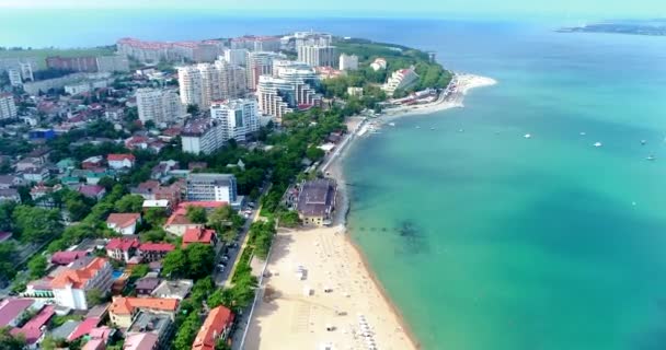 Beach of the seaside city of Gelendzhik in summer. A birds-eye view. Sun loungers and umbrellas on the beach. Emerald water. Yachts at sea. Embankment, trees, hotels and houses on the shore. In the — Stock Video