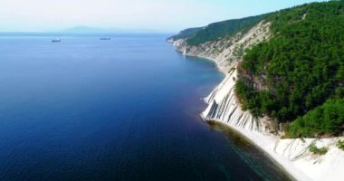 Karadeniz 'in kayalık kıyıları üzerinde uçuş. Çam ağacıyla kaplı, yumuşak dağlar eğimli kayalara dönüşür. Sahilde küçük bir çakıl taşı plajı var. Güneşli bir hava. Uzaktaki gemiler...