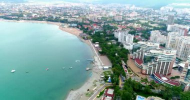 Sahil beldesi Gelendzhik 'in merkez plajı üzerinde uçuş. Güneş yatakları ve şemsiyeli plaj, gezinti güvertesi deniz kenarında, turkuaz su. Deniz kıyısındaki oteller ve kafeler