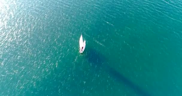Jacht pod żaglami pływa w turkusowym morzu. Zachodzące słońce rzuca długi cień na wodę z żagla. — Wideo stockowe