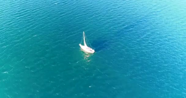 Jacht pod żaglami pływa w turkusowym morzu. Zachodzące słońce rzuca długi cień na wodę z żagla. — Wideo stockowe